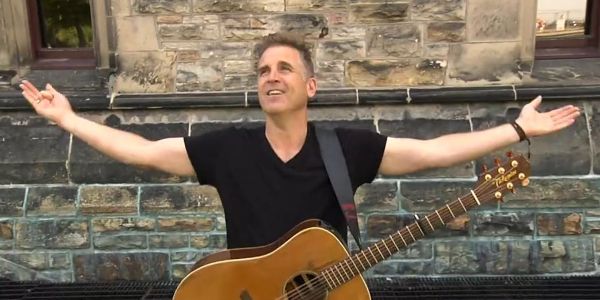 Singer Sean McCann stands with his guitar in front of a building