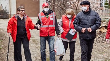 Red Cross staff assist a woman as they walk down a road.