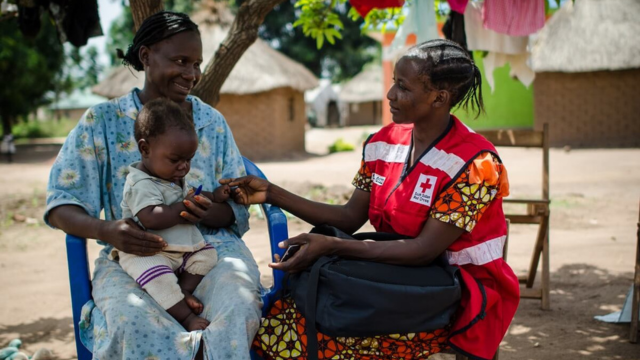 Une personne de la Croix-Rouge du Soudan du Sud discute avec une femme tenant un bébé.