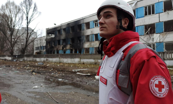 Red Cross personnel standing in front of a damaged hospital.