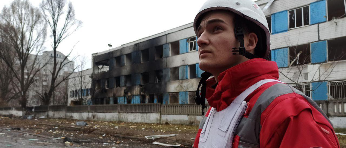 Red Cross personnel standing in front of a damaged hospital.