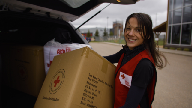 A Canadian Red Cross volunteer holding a large cardboard box with the Red Cross logo on it.