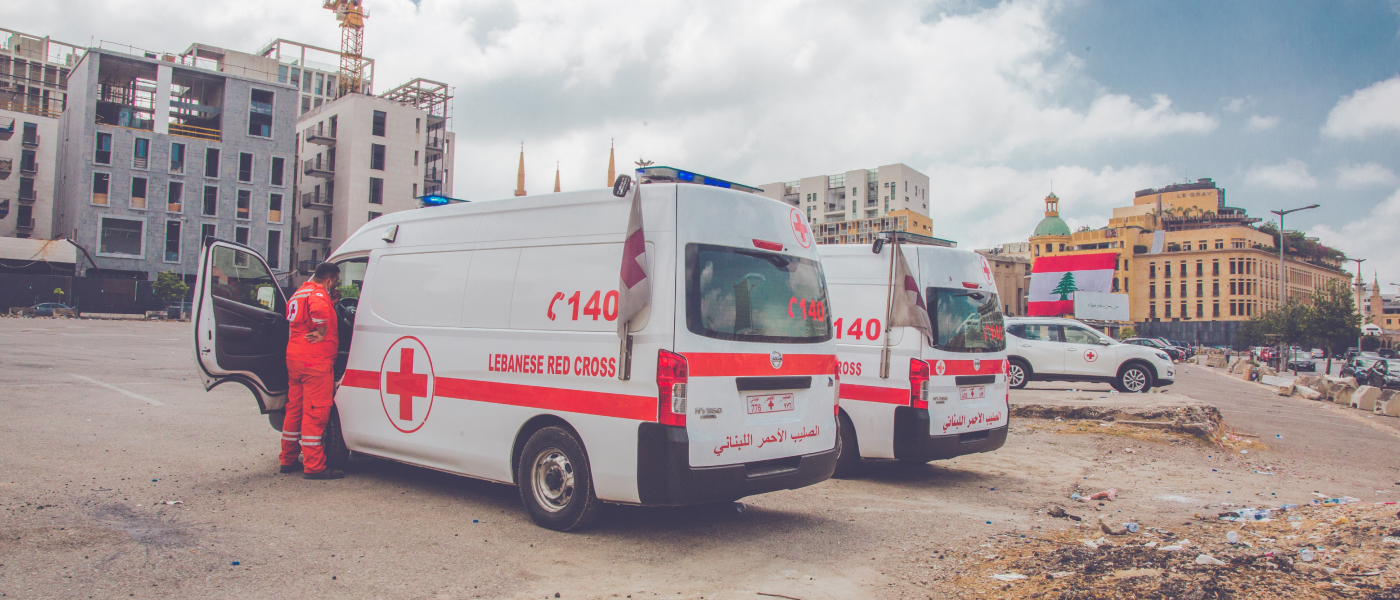 Red Cross personnel standing beside two Red Cross ambulances with cityscape in the background