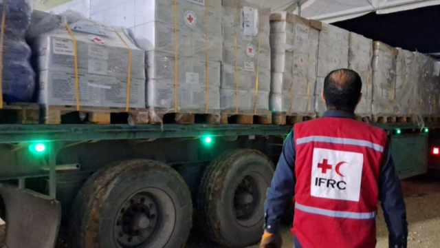 Un membre du personnel de la FICR se tient devant un camion contenant des aides humanitaires.