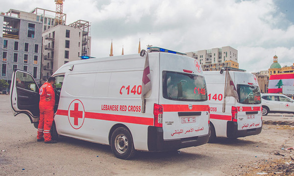 Two large Lebanese Red Cross vans parked in a city among rubble.