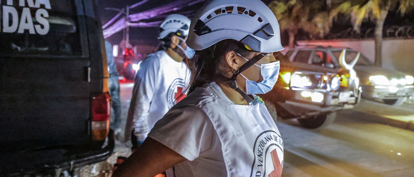 Des membres du personnel de la Croix-Rouge vénézuélienne portant des casques et des masques se tiennent près d’un véhicule pendant l’intervention d’urgence de nuit en réponse aux séismes.
