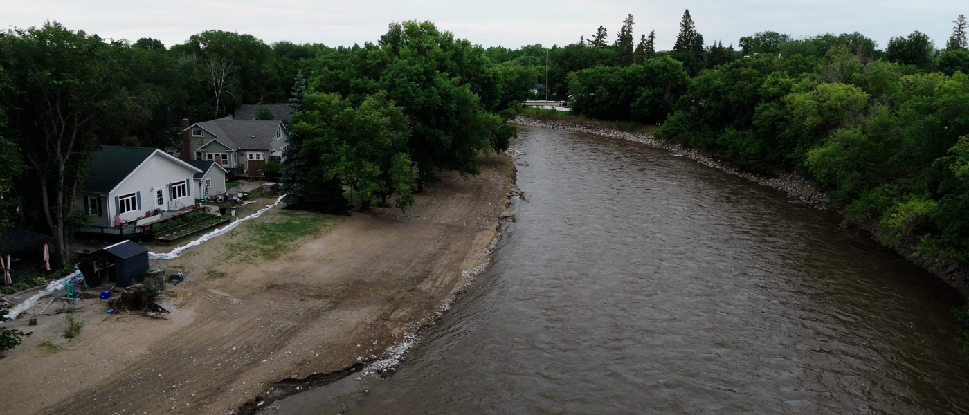 An aerial view of homes with sandbags in front of them beside a river.