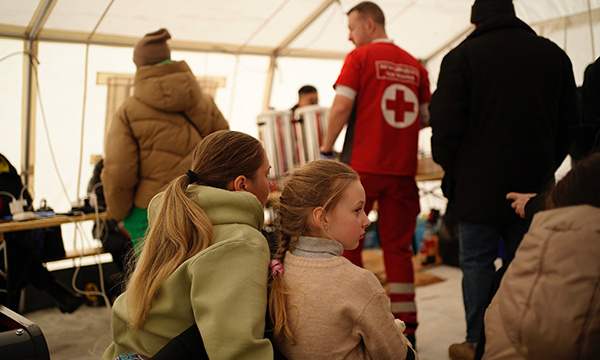 Two children sit and observe activity happening in a winter tent where Red Cross personnel are engaging with people in Ukraine affected by the crisis. 