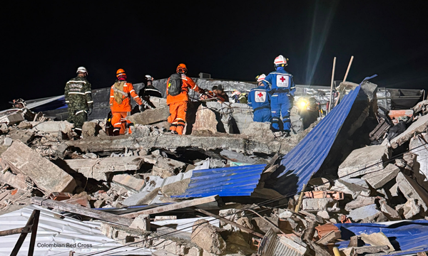 Colombian Red Cross personnel search through rubble with other rescue workers at night.