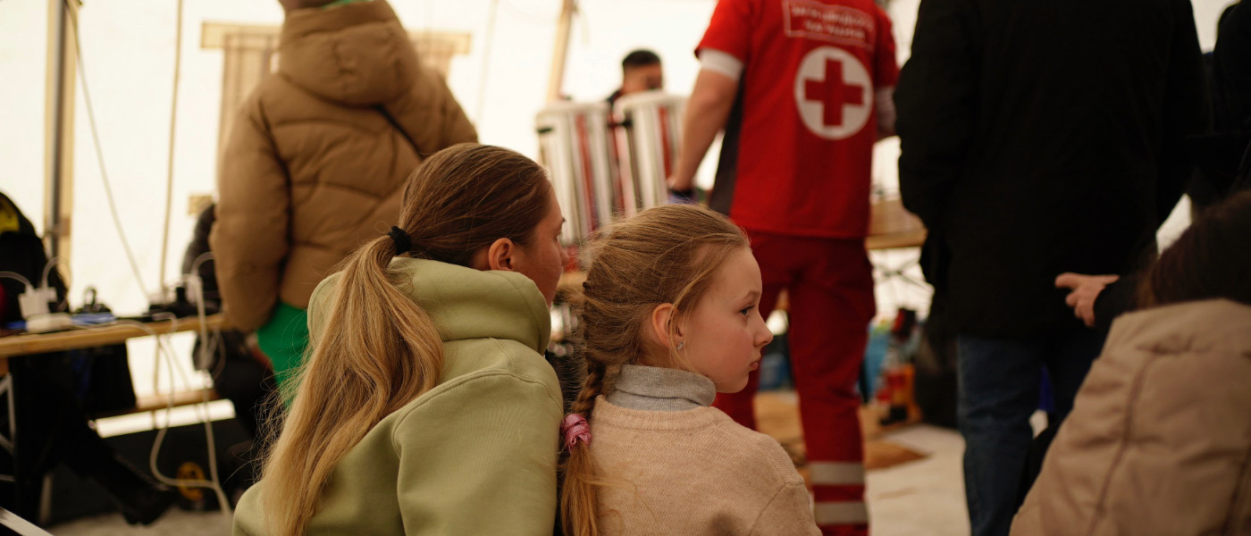 Two children sit and observe activity happening in a winter tent where Red Cross personnel are engaging with people in Ukraine affected by the crisis.  
