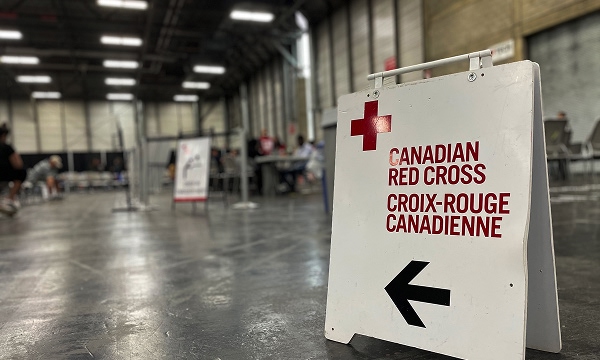 A sign points towards Canadian Red Cross services in a large room, with people waiting the background.