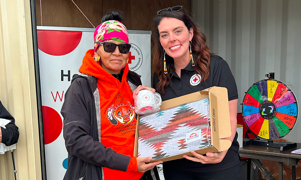 Two smiling women are holding a prize consisting of a folded, patterned blanket and a Red Cross mug.