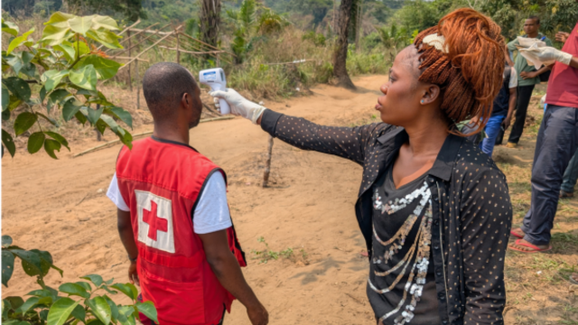 Une bénévole de la Croix-Rouge prend la température d’une personne à l’aide d’un thermomètre lors d’une intervention menée dans une communauté touchée par le virus Ebola.
