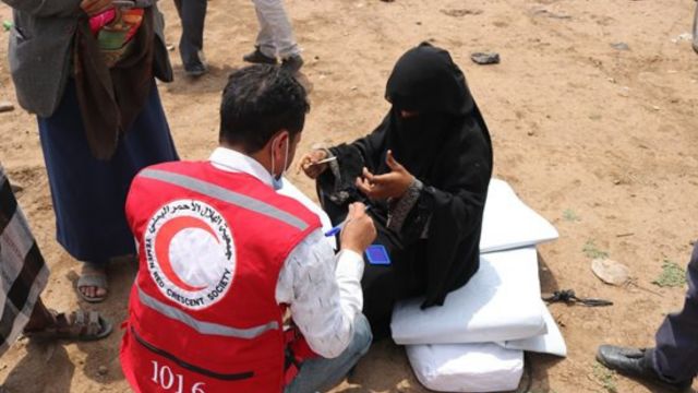 A member of the Red Cross Red Crescent Society kneeling while talking to a person.