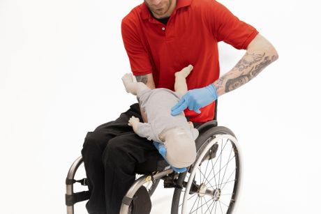 A person in a wheel chair demonstrating chest compressions on a CPR manikin