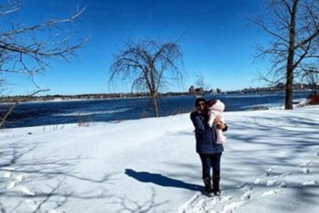 Une femme, portant un habit d'hiver noir, qui tient un enfant dans ses bras, avec un paysage enneigé