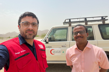 Bahram Ghaemi and a member of the Sudanese Red Crescent Society stand in front of a IFRC vehicle.
