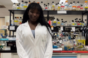 Laura Enekegho est vêtue d’un sarrau blanc et pose devant du matériel de laboratoire.