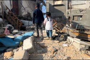 A young boy and young girl hold hands and walk through the remnants of a destroyed building.