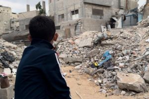 A young boy looks out at the remnants of a destroyed building.