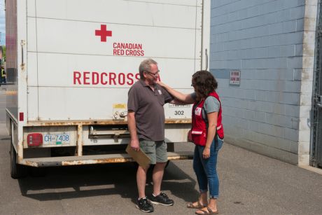 Two people with a hand on each others shoulder, standing in front of a Canadian Red Cross semi-trailer truck