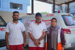 Yehya, Awni, and Tahrer standing in front of a Palestine Red Crescent Society ambulance for a photo.