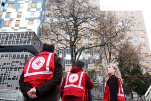 Three Red Cross personnel standing in front of a building, wearing Red Cross vests.