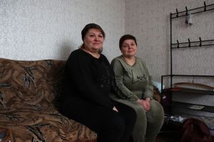 Zhanna Skcola and Svitlana Kovryzhko sit on a couch in their apartment.