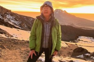 Linda Phillips climbing Mount Kilimanjaro, with a scenic mountain view behind her.