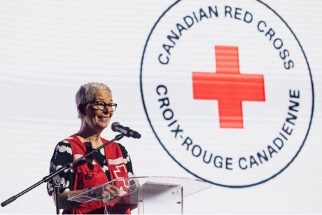 Martine Lalonde stands in front of a podium, with a large Canadian Red Cross logo on screen behind her.