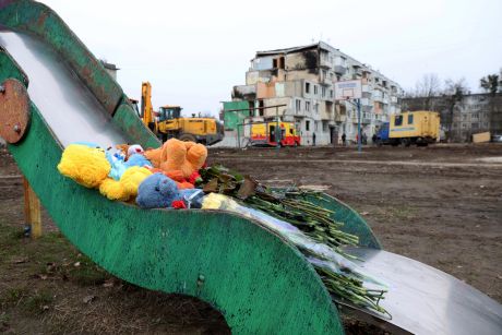 A memorial of flowers and stuffed animals on a playground in front of a damaged building.