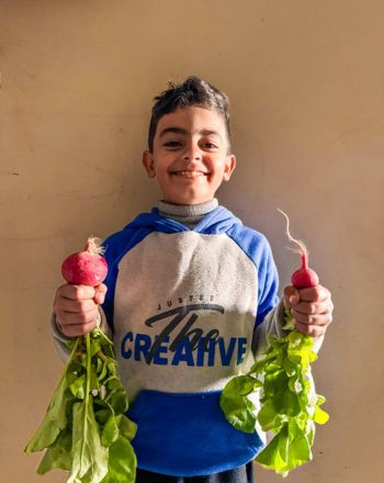 Amr's son smiling while holding vegetables.