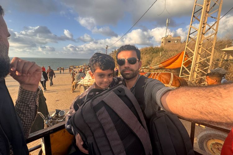 Amr and his son holding a backpack with a beach in the background.