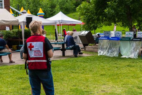 Un membre du personnel porte un dossard de la Croix-Rouge à un événement communautaire dans un parc. 