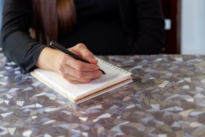 A person writing in a notebook on a countertop.