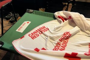 Une couverture rouge et blanche de la Croix-Rouge canadienne étendue sur un lit de camp vert de la Croix-Rouge canadienne.