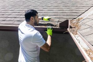 Une personne nettoie les feuilles d’une gouttière d’une maison.