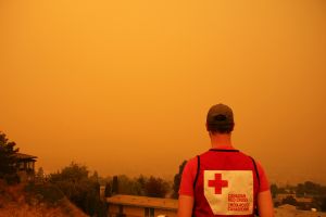 Une personne portant un gilet de la Croix-Rouge canadienne qui observe une communauté enfumée par un feu de forêt.