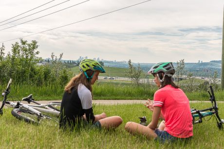 Deux jeunes personnes s’assoient sur la pelouse à côté de leurs bicyclettes. Elles parlent sans enlever leur casque, comme si elles prenaient une pause.