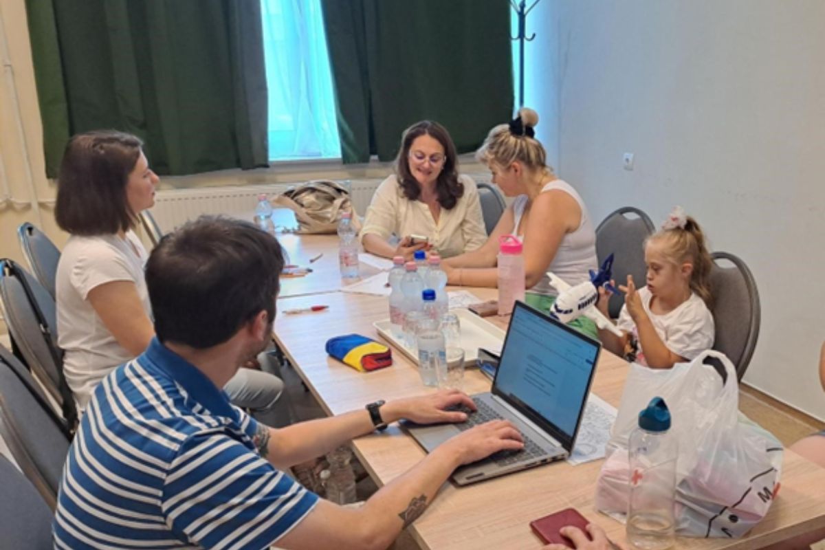 Lana and Anastasia sit in a board room with members of the Red Cross.