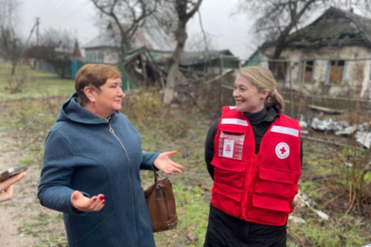Red Cross personnel talks to a woman outside a damaged house.