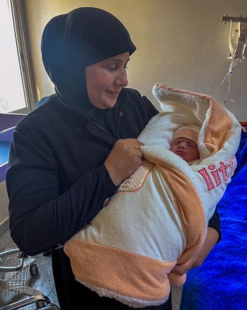 A person holding a newborn baby, wrapped in a blanket.