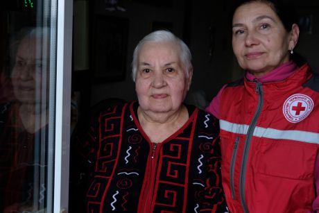 Svitlana and a Ukrainian Red Cross social helper pose for a photo next to a window.