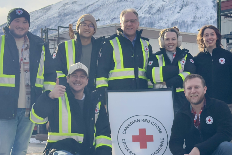 Seven members of the Canadian Red Cross are outdoors, smiling and holding
up a sign.