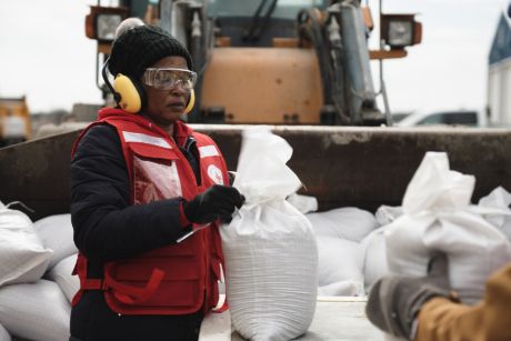 Une bénévole de la Croix-Rouge attache un sac de sable.