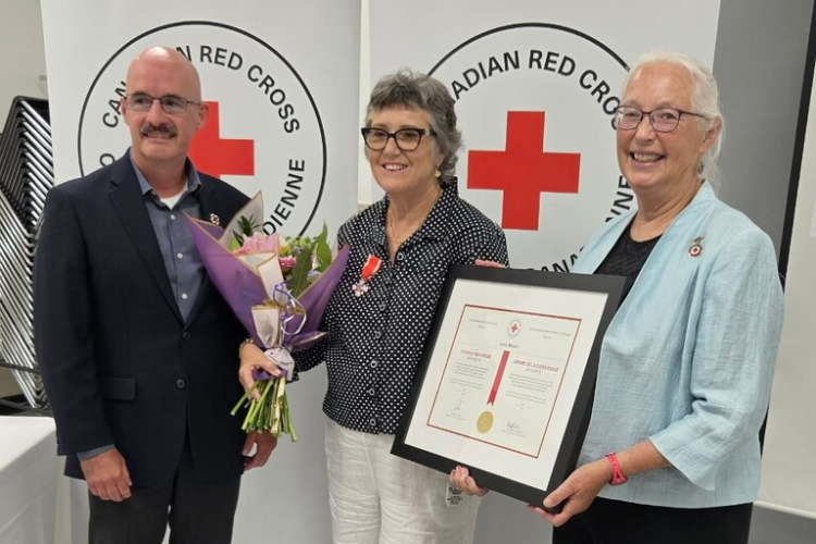 Canadian Red Cross recognition ceremony with volunteer Janis Brown holding flowers and a framed award.