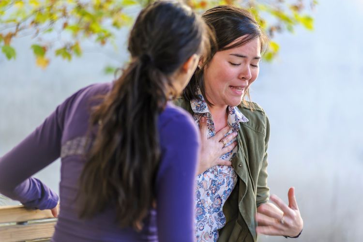 Une personne qui est agitée, se tient poitrine et semble souffrir d’une crise de panique reçoit l’aide d’une autre personne assise avec elle sur un banc de parc.