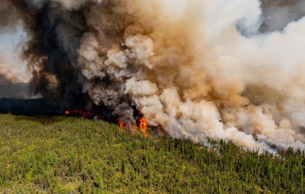 Aerial view of a Manitoba wildfire, showing smoke billowing from trees and a vast landscape affected by flames.