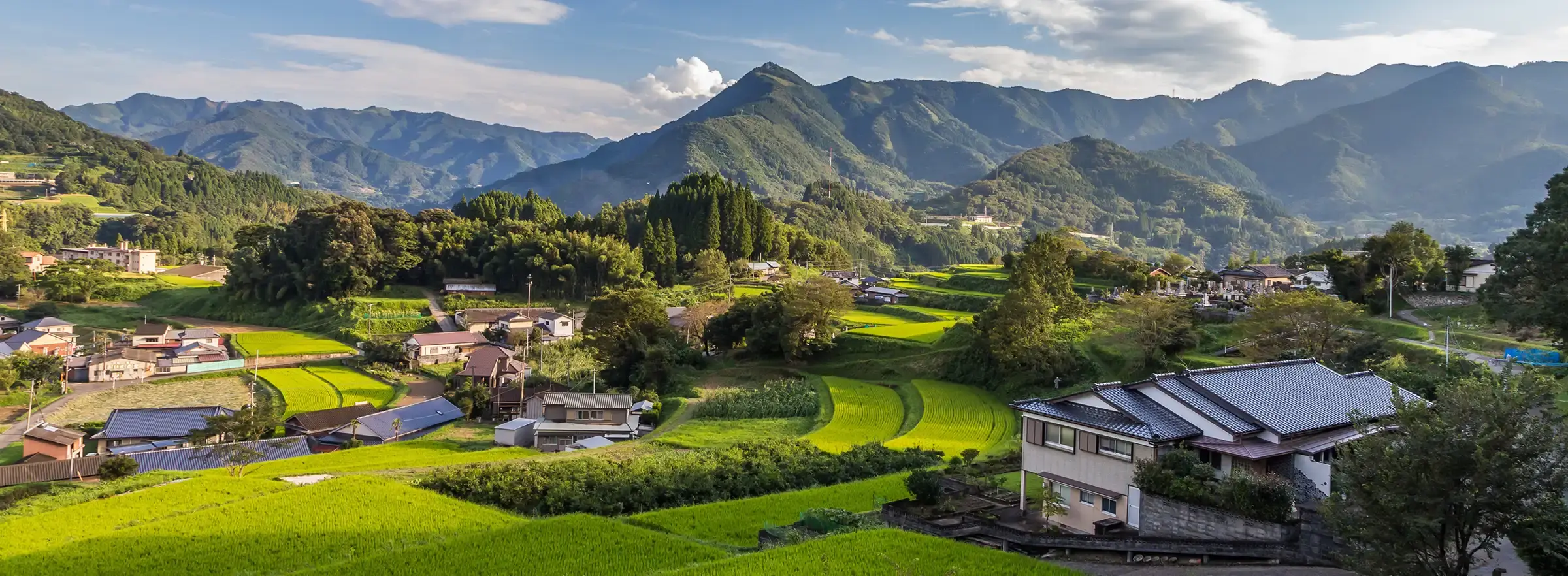 A scenic valley with homes, green spaces, and tree-covered mountains.