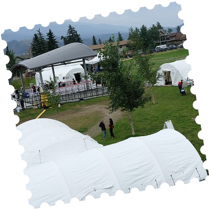 White tents of a Red Cross support centre in a grassy area surrounded by mountains in the distance.